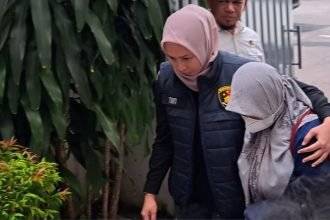 Tersangka Sri Maryani menunduk saat dirangkul penyidik menuju ruang pelimpahan di kantor kejaksaan, Kamis (1552025).