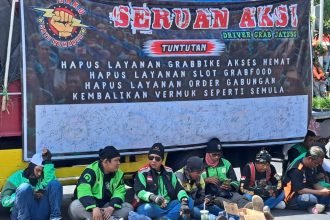Massa aksi demo ojol di Semarang berteduh saat menunggu orator menyampaikan aspirasi.