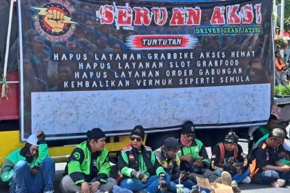 Massa aksi demo ojol di Semarang berteduh saat menunggu orator menyampaikan aspirasi.
