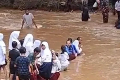 Siswa menyeberang arus sungai yang deras.