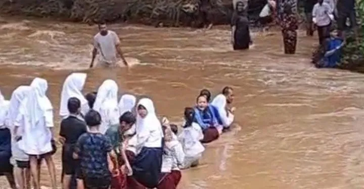 Siswa menyeberang arus sungai yang deras.