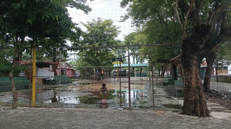 Seorang anak yang lagi mengambil bola dengan berhati-hati karena licin di genangan air yang ada di pinggir lapangan. Kamis (26/3/2026). (dul)