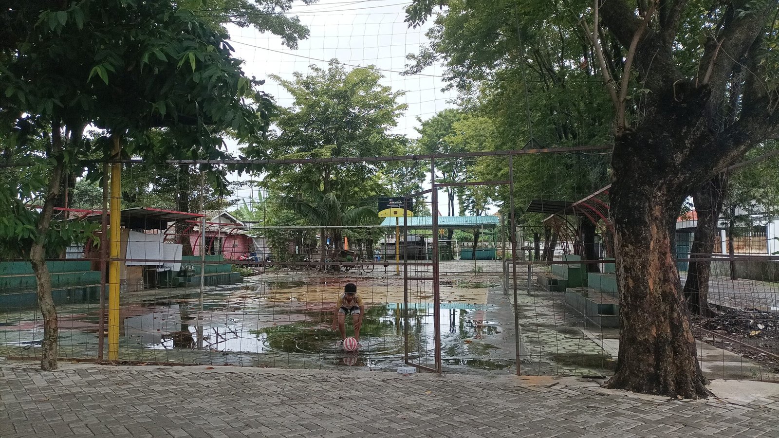 Seorang anak yang lagi mengambil bola dengan berhati-hati karena licin di genangan air yang ada di pinggir lapangan. Kamis (26/3/2026). (dul)