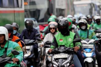 Ilustrasi pengemudi ojek online (ojol) sedang bekerja mengantar penumpang di tengah kepadatan arus lalu lintas kota.