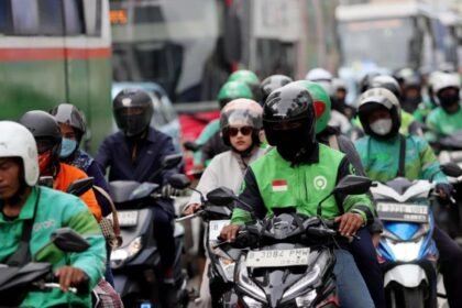 Ilustrasi pengemudi ojek online (ojol) sedang bekerja mengantar penumpang di tengah kepadatan arus lalu lintas kota.