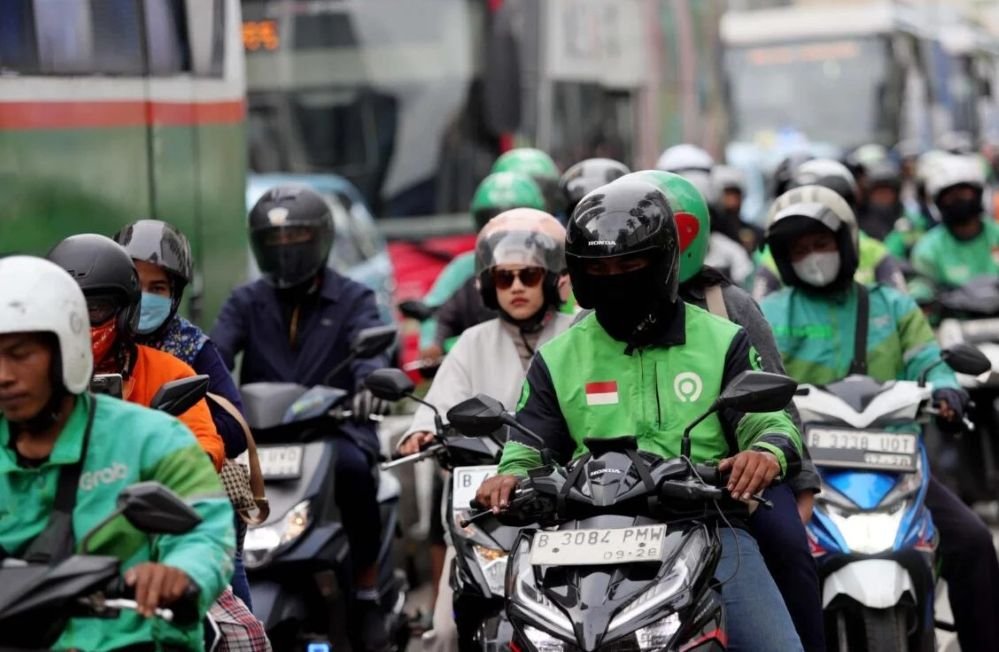 Ilustrasi pengemudi ojek online (ojol) sedang bekerja mengantar penumpang di tengah kepadatan arus lalu lintas kota.
